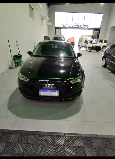 Audi A3 preto parado dentro da Evotek, com o letreiro da loja visível na porta de entrada ao fundo.