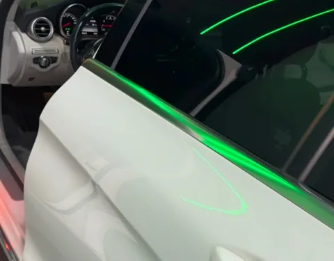 Porta aberta de uma Mercedes C180 na Evotek, com filete de luz verde no vidro. A porta é onde entra a manta de tratamento acústico.